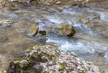 A shallow riverbed with an exposed rocky bottom , a small stream and a stream of water, the spring period in nature