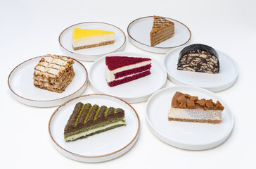 Assorted Slices of Delicious Cakes on White Plates Displayed on a White Background