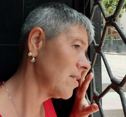A sad woman seen in profile,behind a gate.A depressed woman feeling imprisoned. An adult girl...
