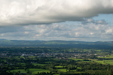 Obraz premium A beautiful wide-angle view of a vast green rural landscape with a small town and wind turbines on distant hills under a cloudy sky