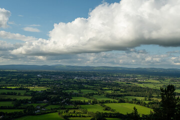 Obraz premium A scenic view of a vast green rural landscape with a town in the distance under a blue sky with dramatic clouds