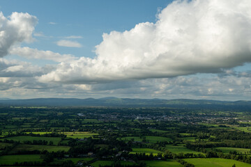 Obraz premium A beautiful wide-angle shot of a green rural landscape with a small town in the middle of the valley under a sky with thick white clouds