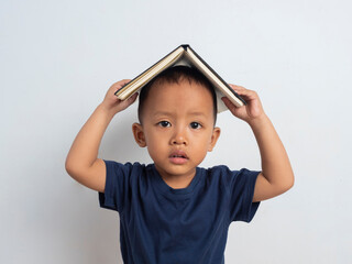 Happy cute and cheerful Asian boy holding a book above his head on an isolated white background....