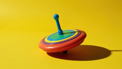 Colorful plastic spinning top toy in motion. Red, orange, yellow, blue, green, purple rings on toy. Isolated on bright yellow background. Fun childhood game.