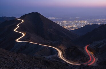 Zigzag mountain road features car light trails at dusk in Al Hada, Taif, Saudi Arabia. Illuminated city lights glow below rocky landscape as vehicles create streaks of light on winding highway,