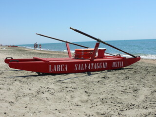 Obraz premium Red lifeguard boat on sandy beach in Ostia, Italy. Calm summer day, blue sea and clear sky in the background. Ideal for travel and vacation themes.