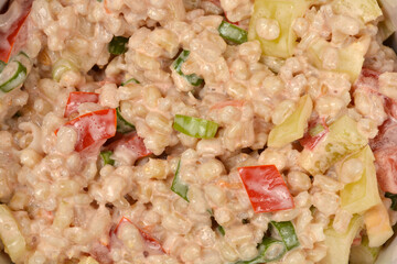 A close-up, top-down view captures the rich texture and vibrant colors of a barley salad, featuring diced peppers, tomatoes, and green onions mixed in a creamy dressing