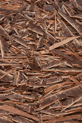 A rich, textured close-up captures a chaotic pile of dark chocolate shavings, perfect for dessert toppings or baking