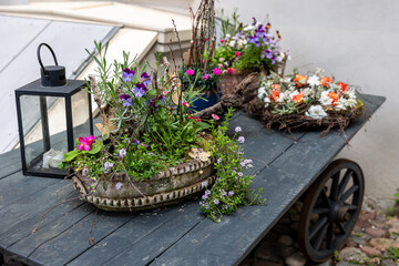 Still life shows flowers in baskets arranged on rustic cart