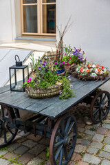 Still life shows flowers in baskets sitting on rustic cart