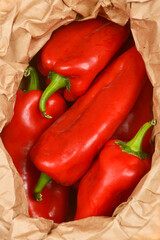 This close-up image shows red bell peppers gathered in a crumpled paper bag, ready for cooking