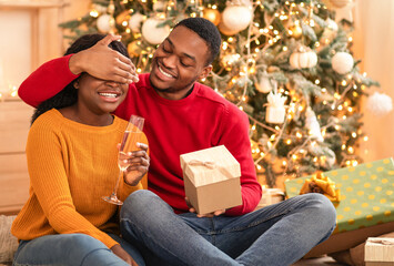 Presents time in living room. Smiling young african american husband closes eyes to woman with...