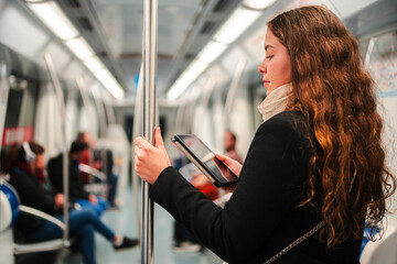 Fototapeta premium Engaged woman concentrated on her e-reader while standing in a subway train, fully absorbed in the digital content as she holds onto a pole for support during her daily transport journey in the city