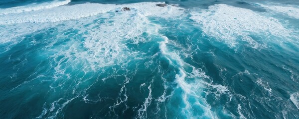 Aerial view of deep blue ocean waves crashing onto shore, creating white foam and spray. Bird eye perspective captures dynamic seascape with turquoise water and clear sky.