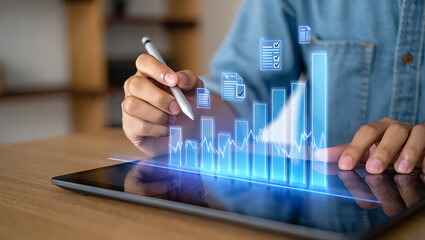 Person using stylus on tablet displaying glowing blue financial charts and documents graph data