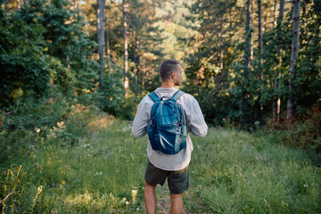 Young male hiker with backpack exploring forest trail enjoying the tranquility of nature during summer hike