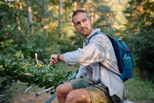 Young male hiker checking the time on his smartwatch while taking a break during a trek through a peaceful forest setting