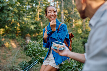 Young woman receiving a lunch box containing nuts and dried fruit from her hiking partner, during a break in the woods