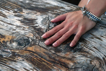 Close-up of a delicate hand resting on weathered wood, adorned with an elegant pearl and silver bracelet featuring intricate details
