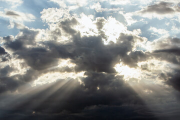 Dramatic sky with dark, billowing clouds illuminated by sunlight, creating a striking contrast and...