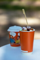 vibrant, colorful dessert served in an orange paper cup, topped with powdered sugar and variety of mini marshmallows, creating playful and indulgent treat