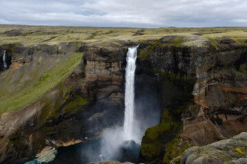 Haifoss waterfall cascading down rugged cliffs in Icelandic landscape under a cloudy sky