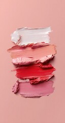 A vertical arrangement of various shades of lip product swatches.  Brushstrokes create textured, flowing lines.  Pale to deep pink and red hues.  Pastel color palette on a blush-toned backdrop