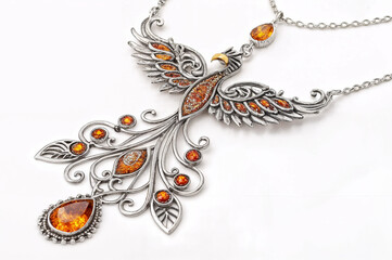 Fototapeta premium delicate silver necklace pendant with intricate filigree designs and an oval amber-colored gemstone at its center. The pendant is set against a plain white background.