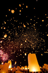 sky lanterns fly into the night sky during yi peng festival with fireworks in the background, loy krathong and candlelight processions, Chiang mai