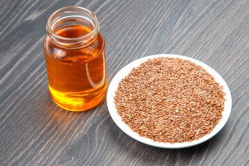 Flaxseed oil in a jar beside a bowl of whole flaxseeds on a wooden table