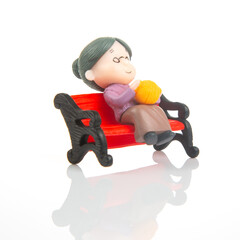 Miniature woman knitting on a red bench during a quiet afternoon