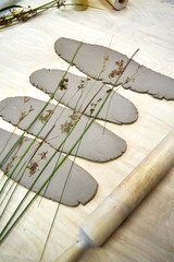 Pressed plants laid over rolled clay sheets, creating organic textures for handmade napkin rings. A...