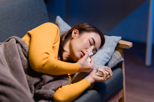 Asian Woman Sick with Cold or Flu Lying on Sofa Using Tissues Nasal Congestion Allergies Runny Nose Rest at Home Remedy Relief Healthcare Concept