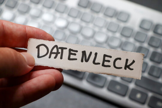 Hand holding a note with the word datenleck against a blurred computer keyboard, highlighting concerns regarding data breaches and cybersecurity issues.