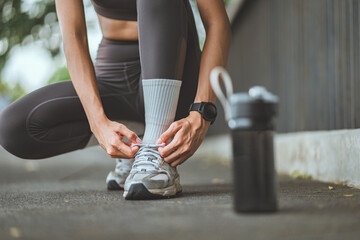 Close up of female runner tying shoelaces on running shoes for a summer jog in a forest park, with a reusable water bottle beside – fitness motivation, healthy lifestyle, and outdoor exercise routine