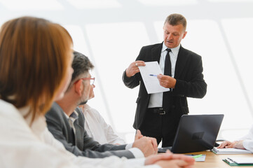 Senior businessman leading a meeting, explaining statistics to colleagues