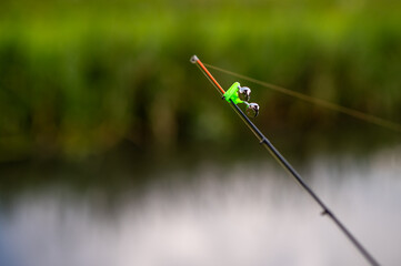 Fishing rod tip with bell bite alarm on blurred water background