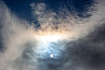 Colorful clouds surround bright sun during late afternoon in a clear sky