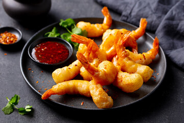 Tempura shrimp with chili sauce on a black plate. Dark grey background. Close up.