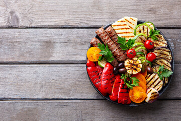 Kebab and halloumi cheese with vegetables on a plate. Wooden background. Close up, copy space. Top...