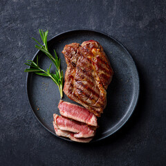 Steak medium rare on a black plate. Dark grey background. Close up. Top view.