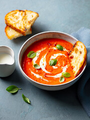 Tomato soup with cream in a white bowl on grey stone background. Close up.