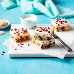 Blondie dessert. White chocolate brownie with cranberries. Blue background. Close up.