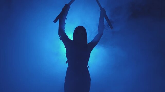 Dark black silhouette fantasy woman warrior assassin holding two katana swords. Black background blue neon light full smoke. Fairy soldier girl hand raised. Armed sexy girl princess. Medieval weapon