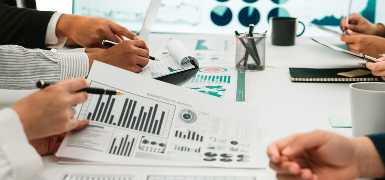 A diverse business team engages in a collaborative meeting focused on data analysis and strategic planning, surrounded by charts, graphs, and interactive reports. SACTR - Powered by Adobe