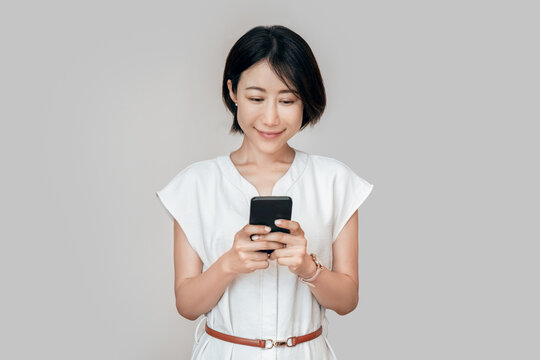 Asian mature business woman manager ceo using cell phone mobile app. Smiling eastern young businesswoman holding smartphone cellphone device for trading, banking, working online. Isolated portrait