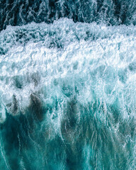 Aerial drone view of ocean surf crashing onto the shore. Turquoise water with white foam creates abstract natural patterns – a dynamic top-down shot of waves and sea textures.