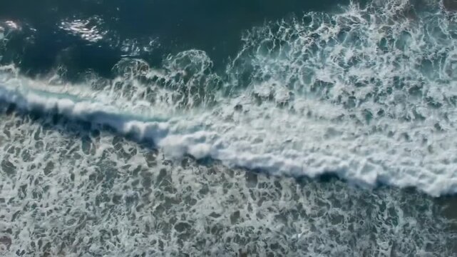 Aerial view of ocean waves crashing and foaming on the surface of the dark water