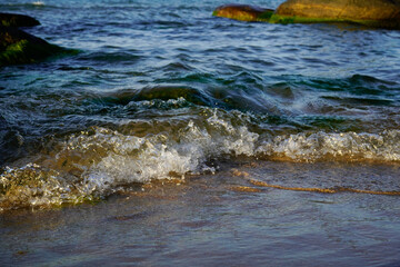 Calm waves meet a sandy beach with rocks in the background, view of the Baltic Sea near the North Perd in 18586 Göhren, island of Rügen, Germany