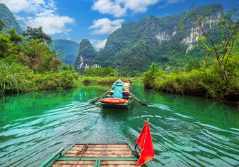 Beautiful landscape view of a touristic and traditional boat sailing through Tr&agrave;ng An karst landscape in Vietnam on a sunny day